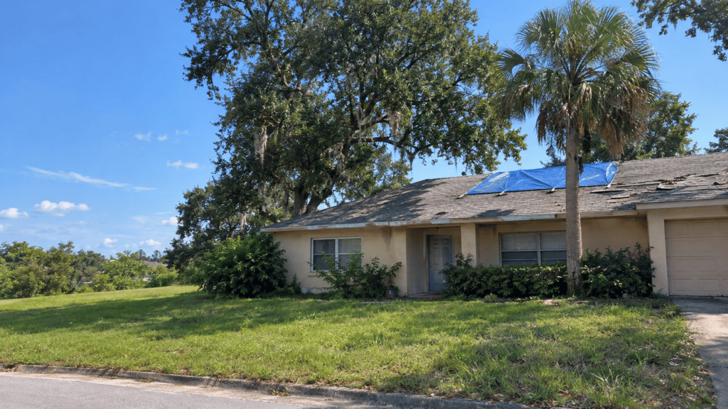 A Central Florida house that needs repairs with a tarp on the roof